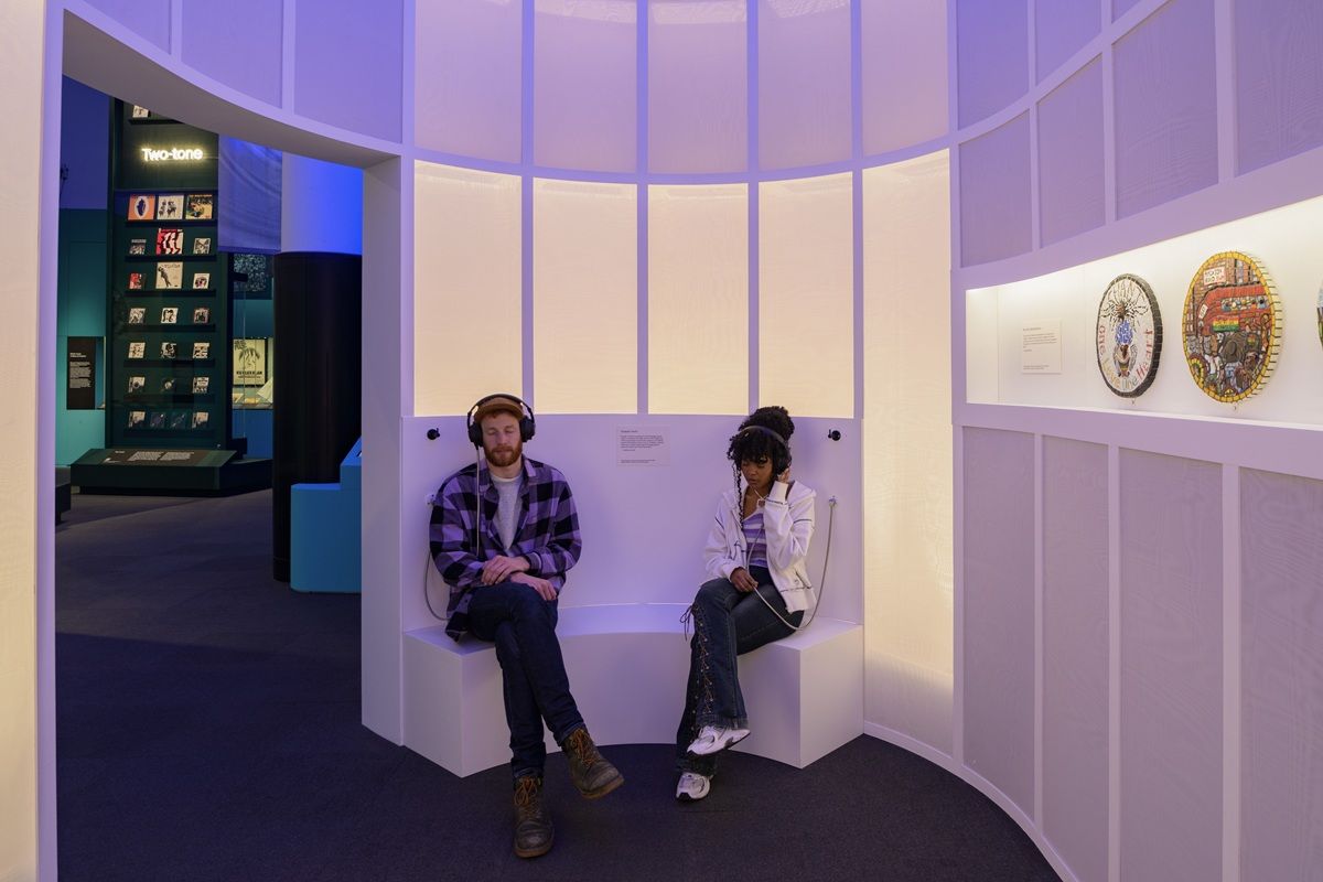 Two people sat in the Beyond the Bassline exhibition with headphones on. 