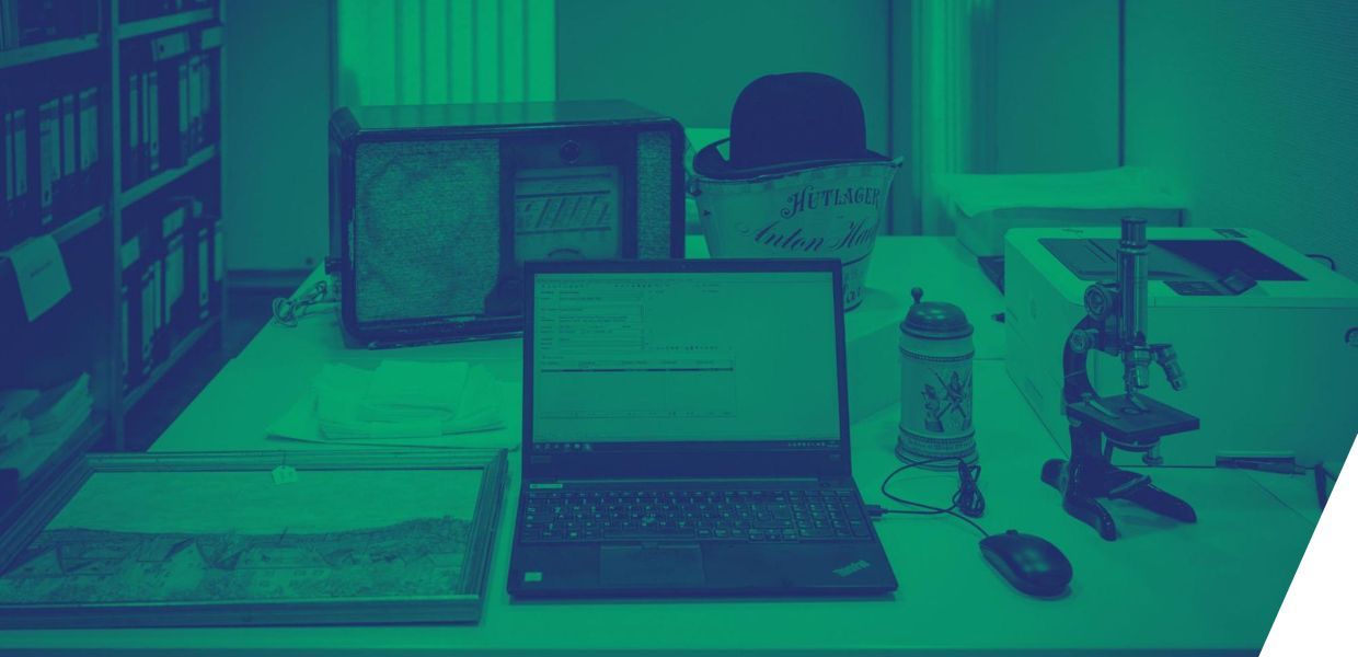 A painting, computer, a beer tankard, a bucket and a hat laid out on a table