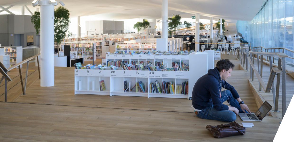 A student sat on the floor working on his computer in a library
