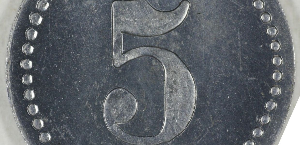 A close-up of a metal coin with the number 5 embossed in the center. The edge of the coin is decorated with a dotted border. The surface shows signs of wear and age.